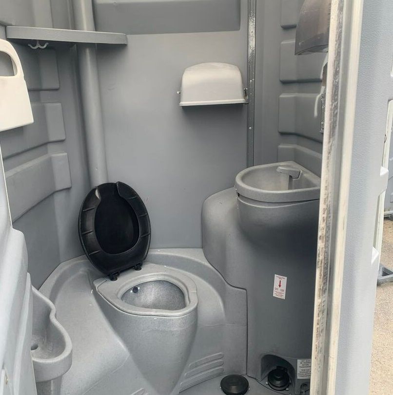 Portable toilet interior with gray walls, open black seat, and sink on the right