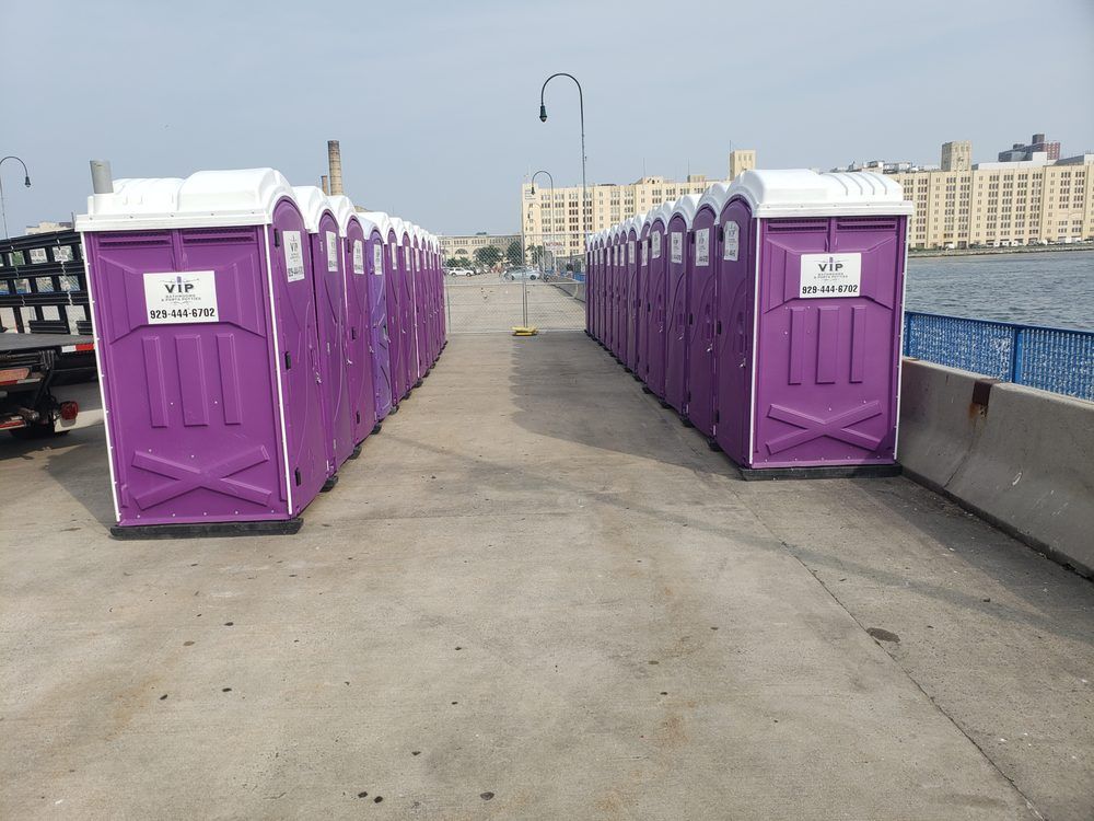Rows of purple portable toilets line a waterfront pier under a cloudy sky.