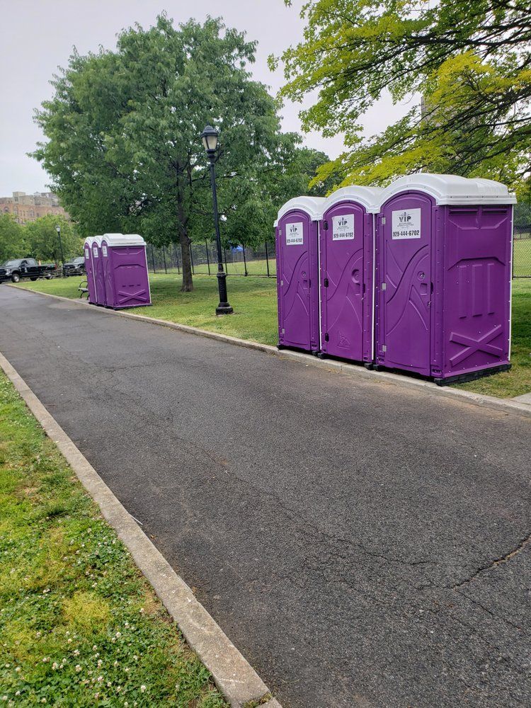 Purple portable toilets along a park path beside trees and grass