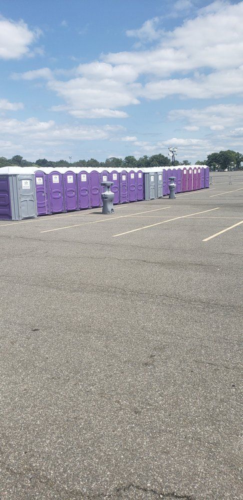 Row of purple portable toilets on an empty paved lot under a partly cloudy sky