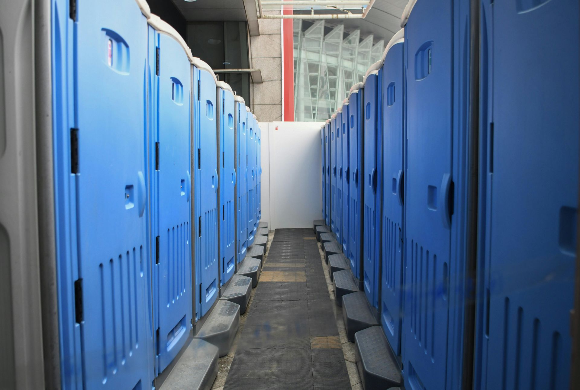 Blue portable toilets lined up in a narrow outdoor corridor under a covered structure