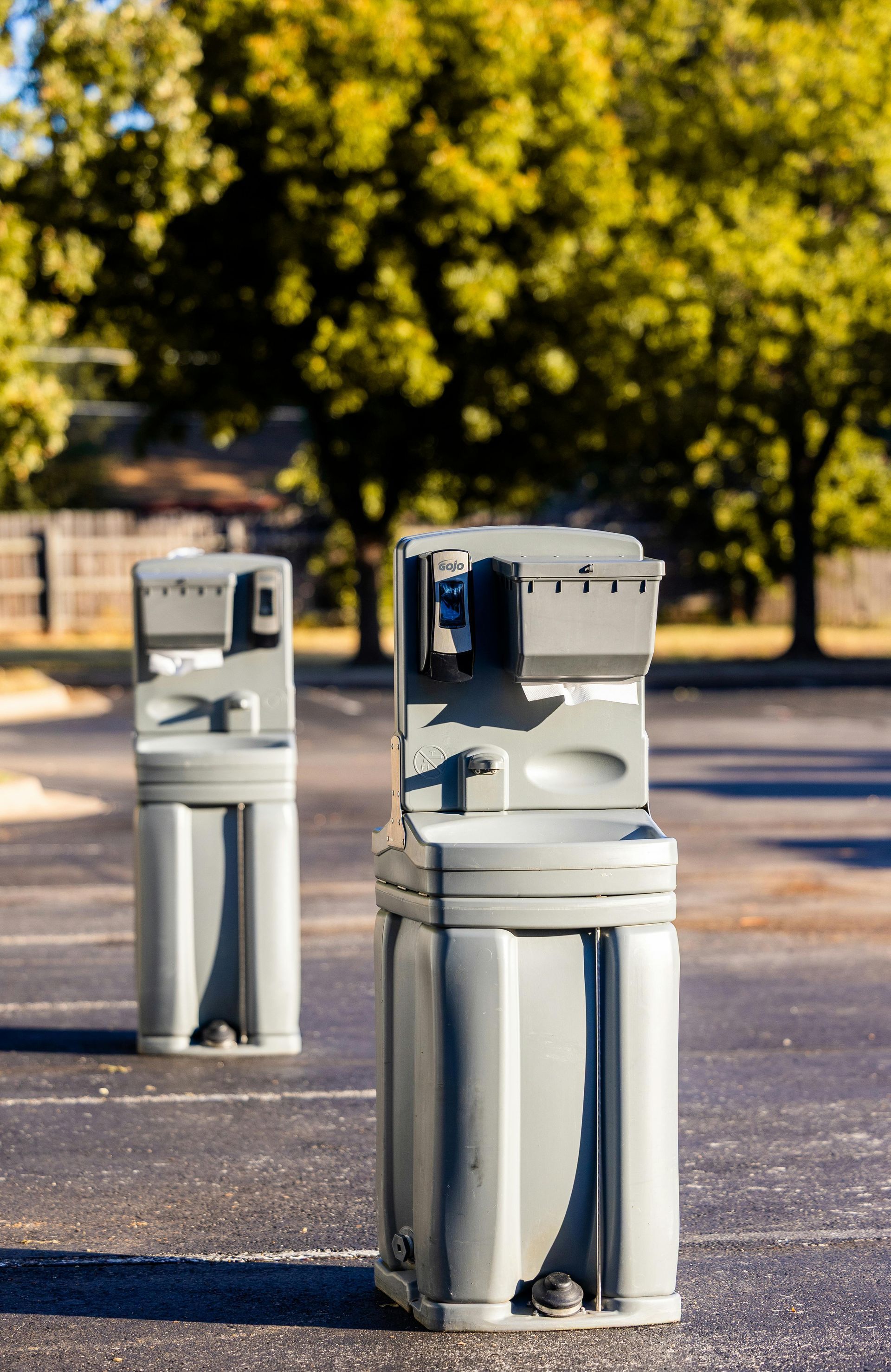 Three stainless-steel bollards on a paved path with trees in the background.