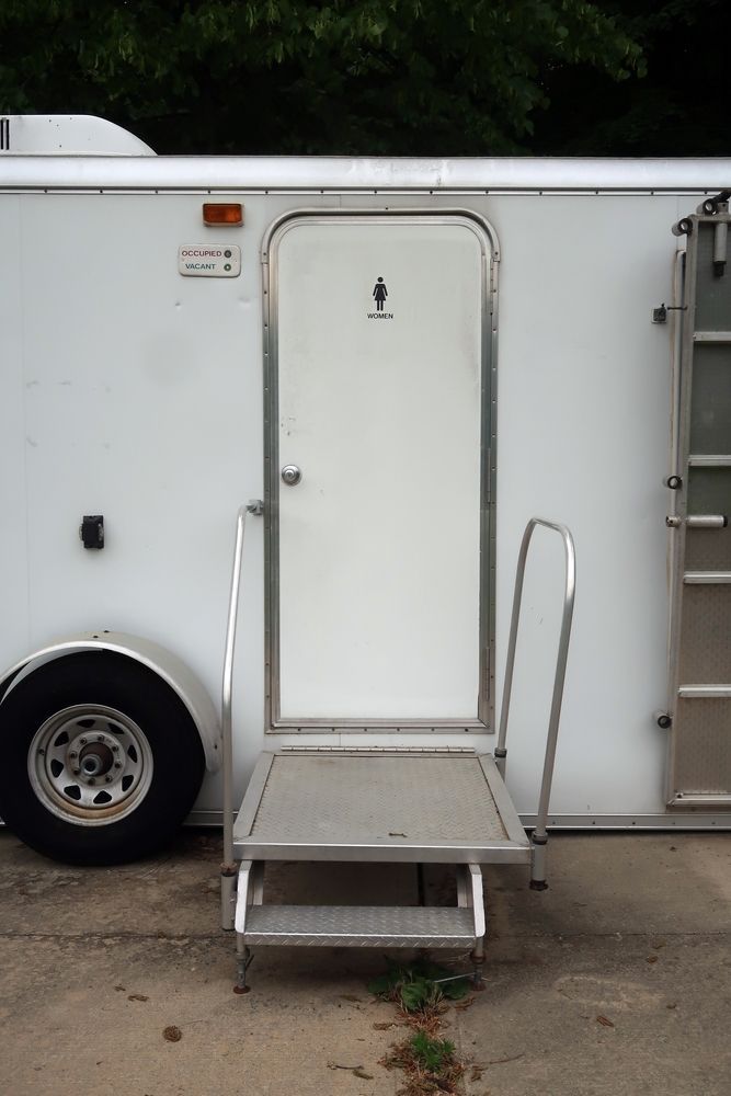 White trailer side door with small metal steps and rail, parked outdoors.