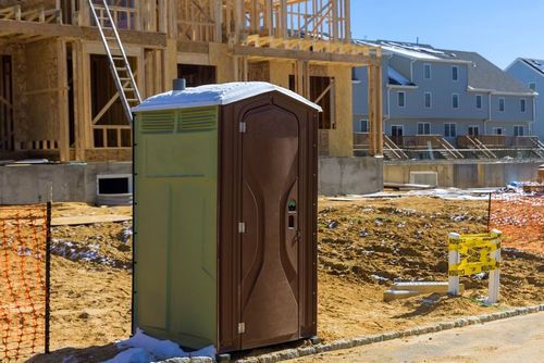 Portable toilet at a construction site with wooden framing and houses in the background