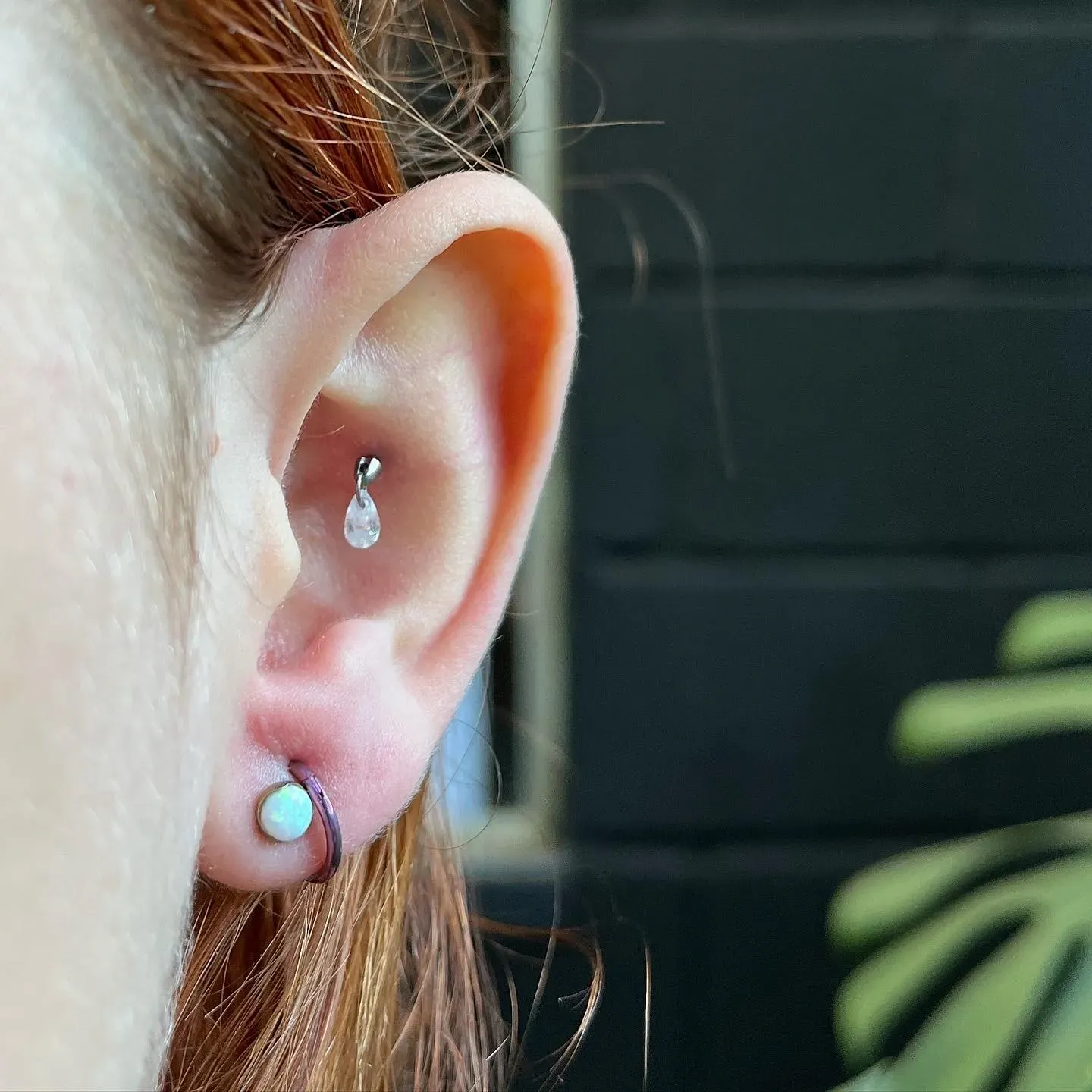 Detalhe da orelha com dois piercings, um no lóbulo e outro na parte superior da orelha.