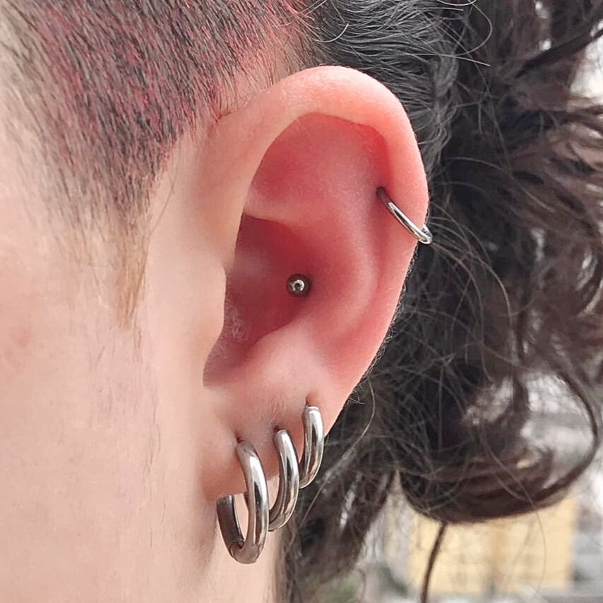 Close-up da orelha com múltiplos piercings: hélice, tragus e três argolas no lóbulo inferior.