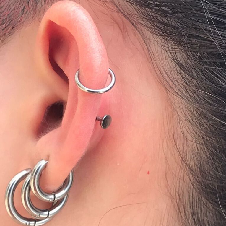 Detalhe de uma orelha com vários piercings: argolas sobrepostas, uma argola na cartilagem e um brinco de pino com base plana.