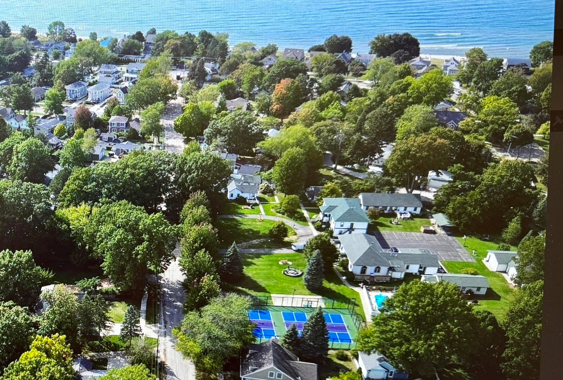 Aerial view of a coastal neighborhood with green trees, houses, and the ocean in the background