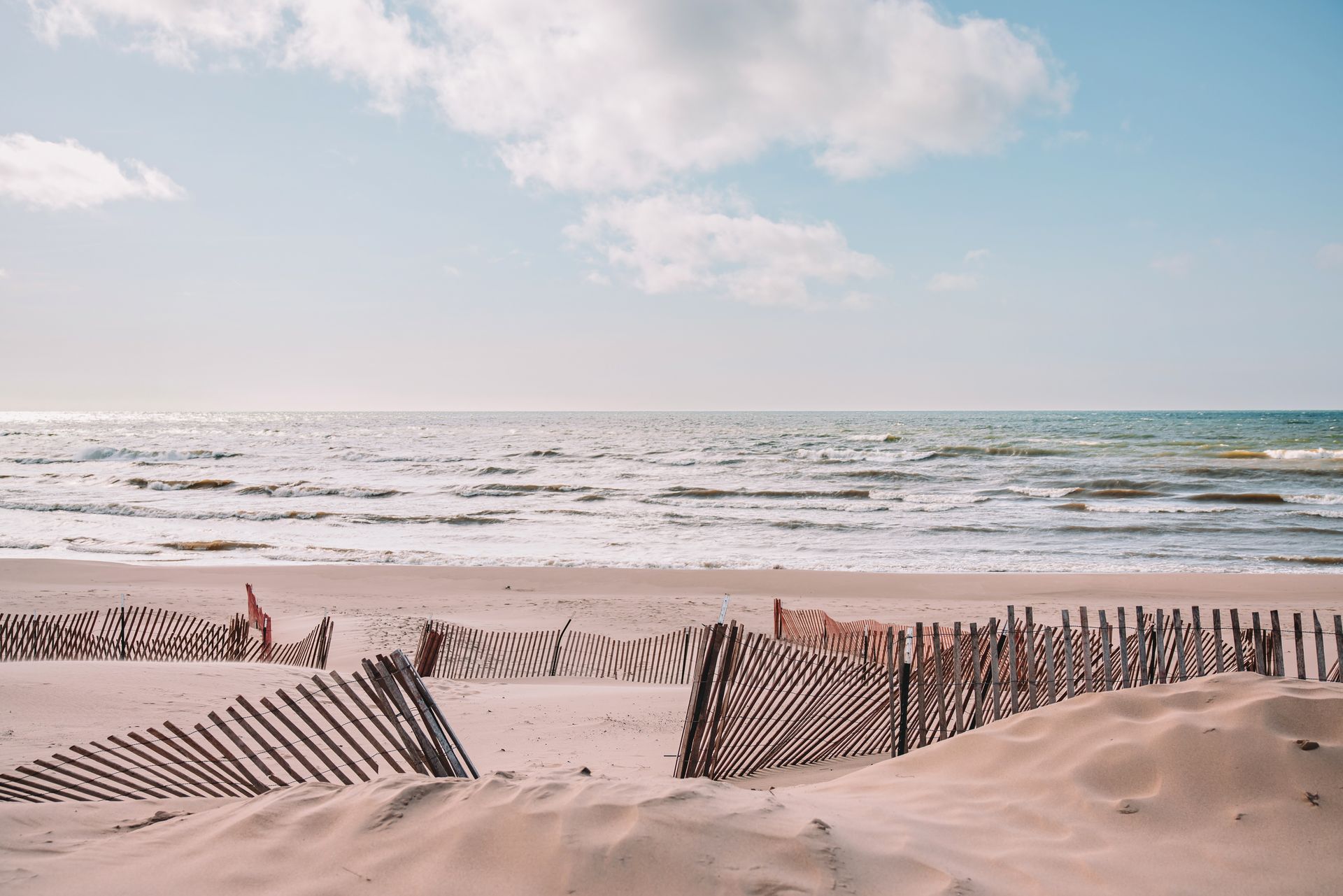 Sandy beach with ocean waves, wooden fence, and a pastel sky at sunrise or sunset