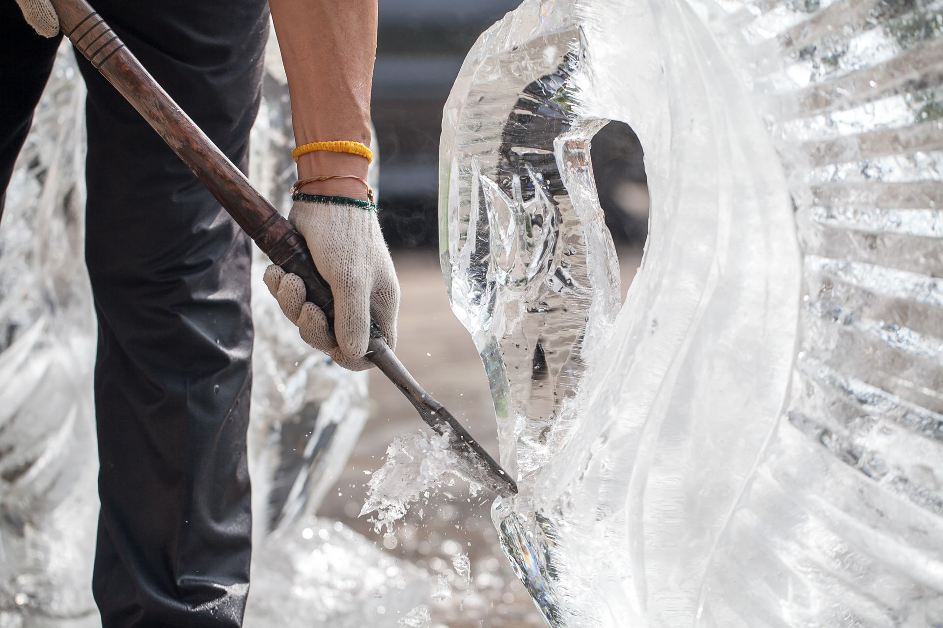 Gloved worker chiseling a large transparent ice sculpture in a workshop