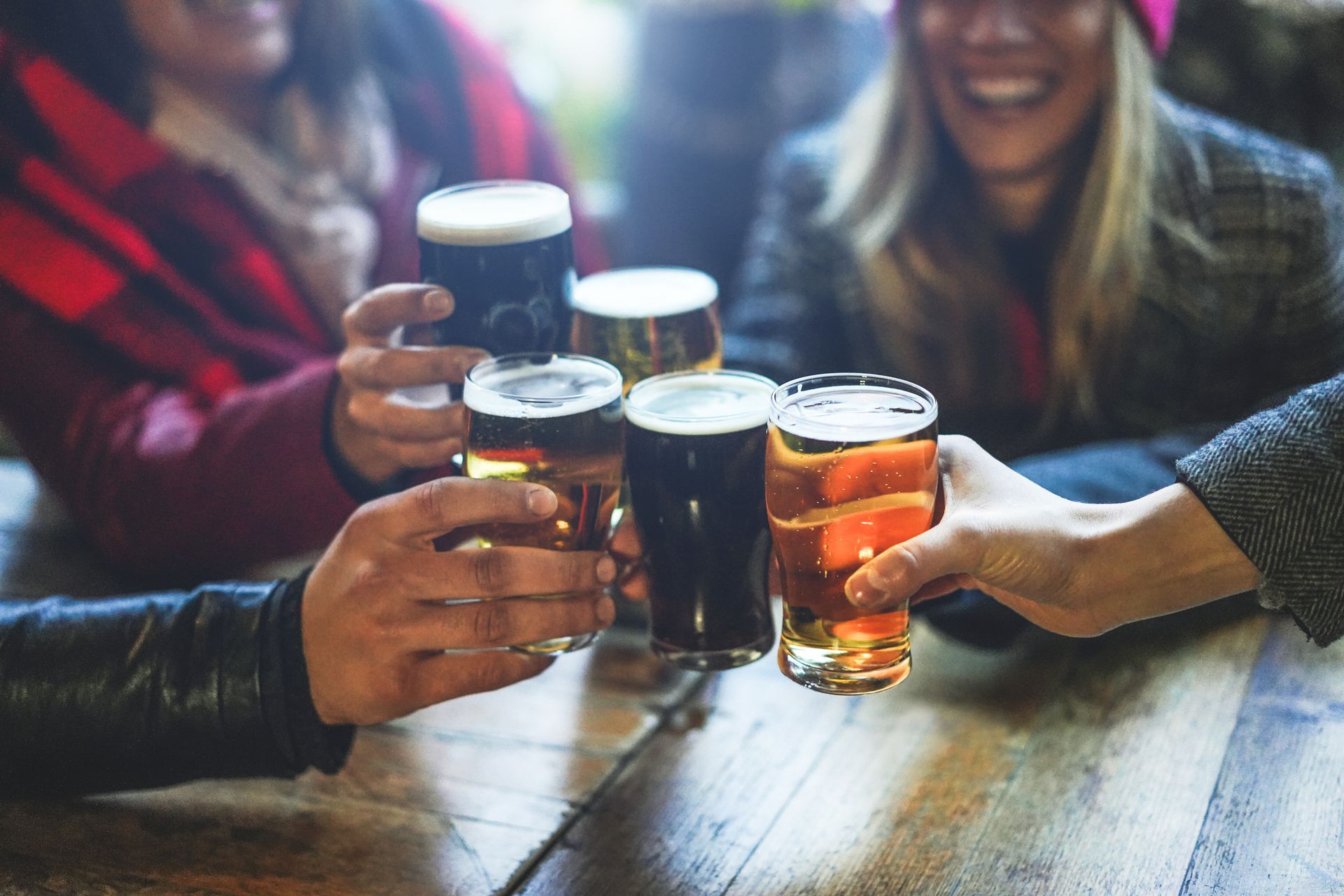 Friends clink beer glasses around a wooden table in a cozy pub.