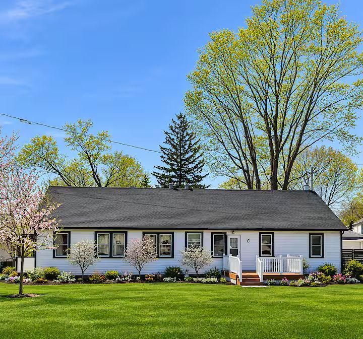 Single-story white house with dark roof, front steps, and a large green lawn under a clear blue sky