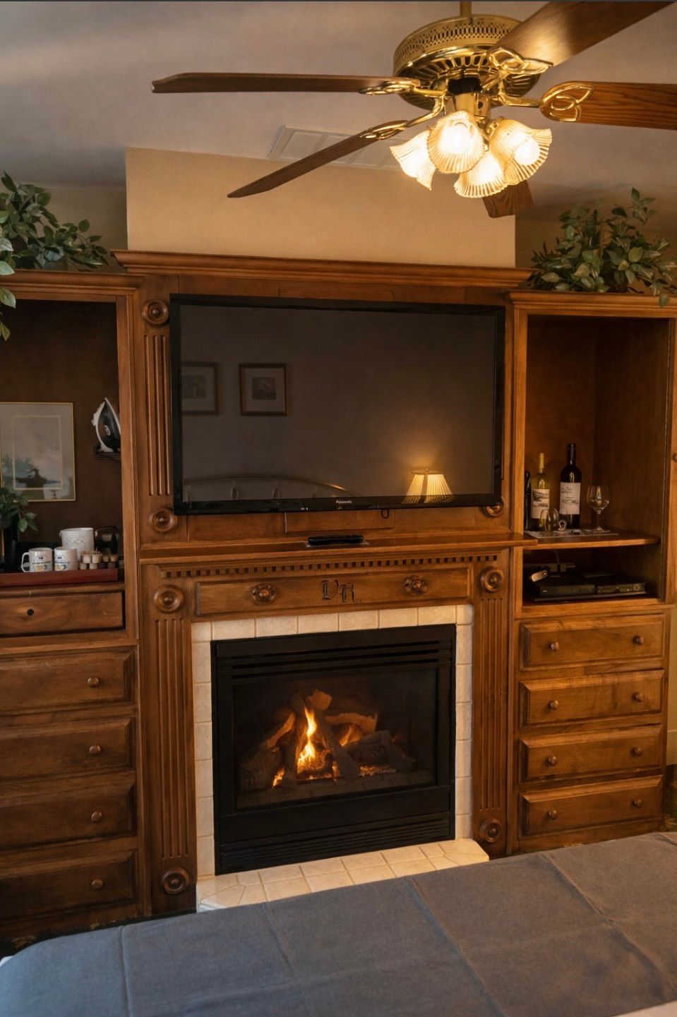 Living room fireplace and built-in wood cabinets with TV, lit fire, and ceiling fan overhead