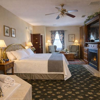 Cozy hotel bedroom with a king bed, fireplace, desk, and floral window drapes
