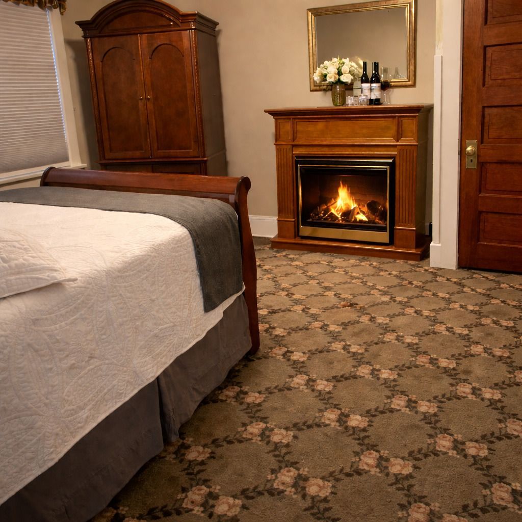 Bedroom with a bed, wooden armoire, and lit fireplace over patterned carpet