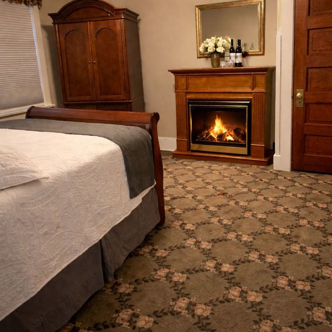 Bedroom with a bed, wooden armoire, and lit fireplace over patterned carpet