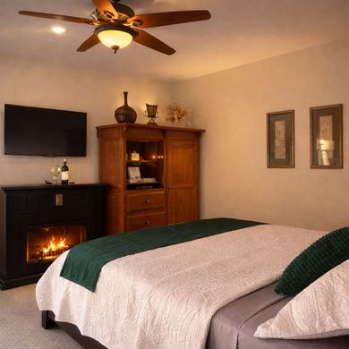 Cozy bedroom with a fireplace, wall-mounted TV, ceiling fan, and a bed with green blanket accents