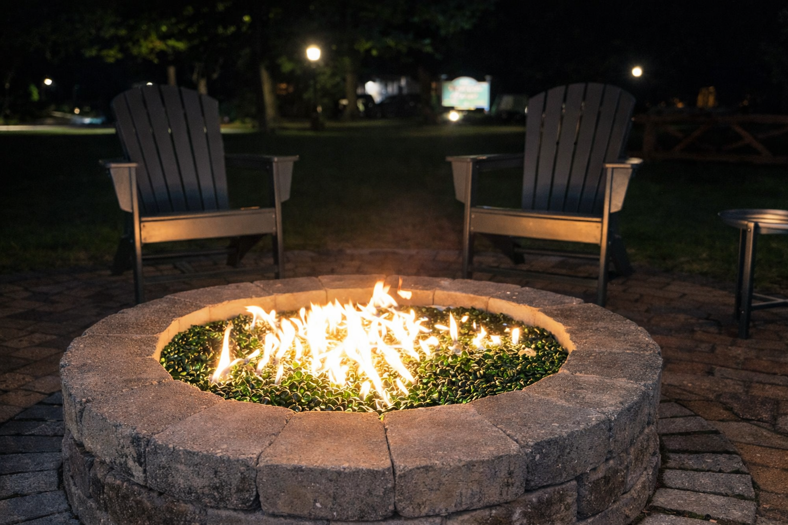 Stone fire pit with bright flames between two wooden chairs outdoors at night