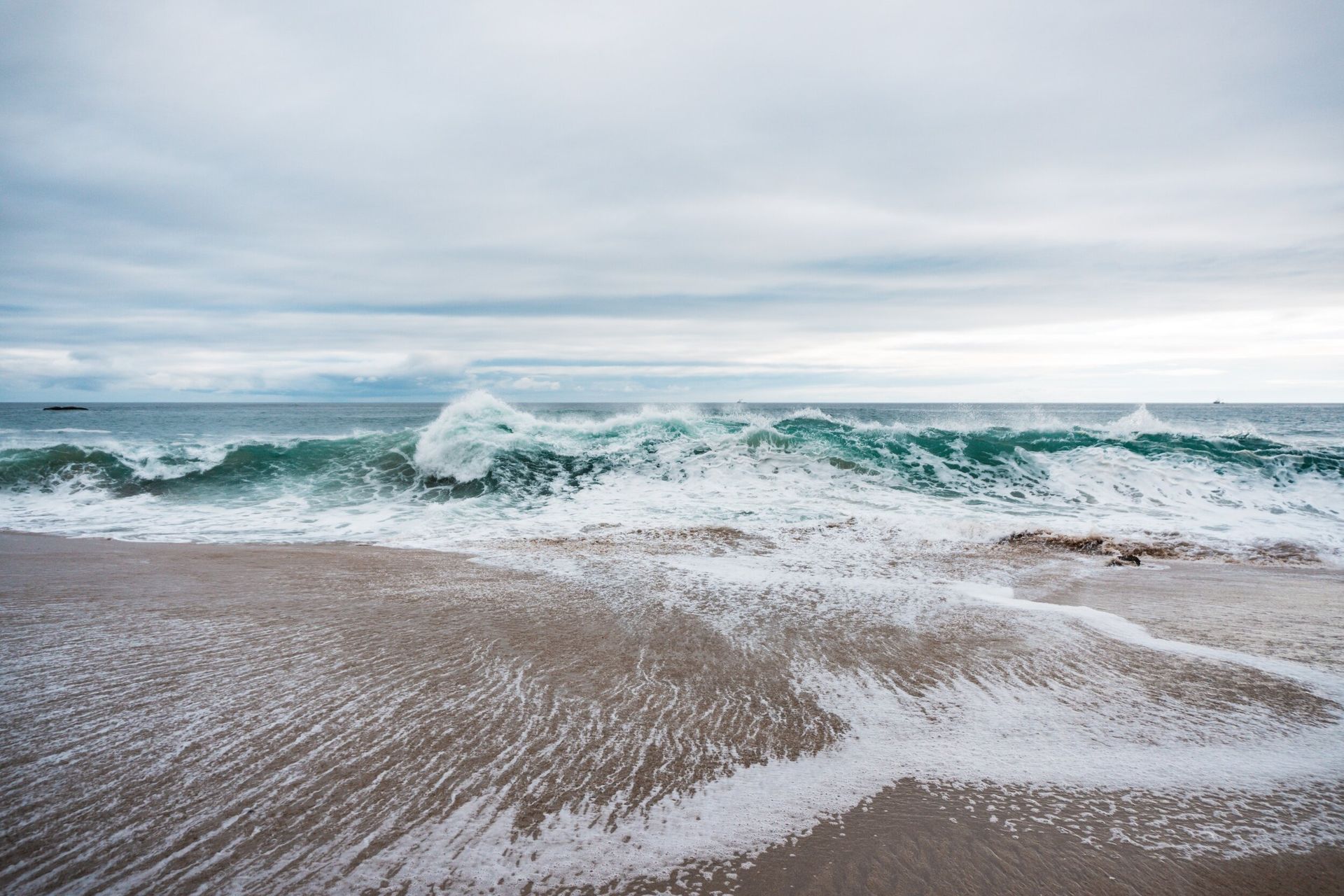 Waves breaking on a sandy beach under a cloudy sky
