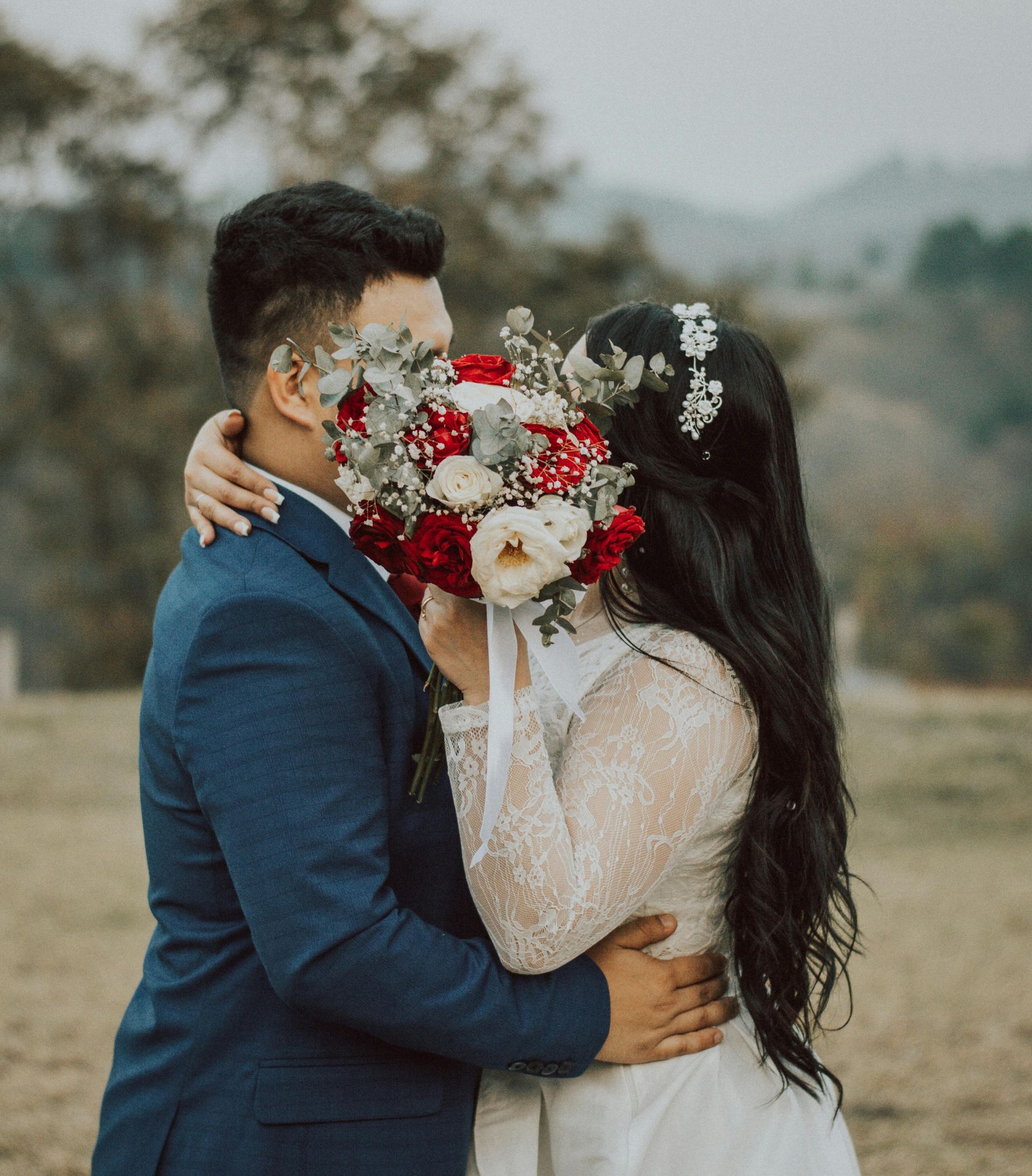 Couple embracing outdoors, faces hidden behind a bouquet of red and white flowers