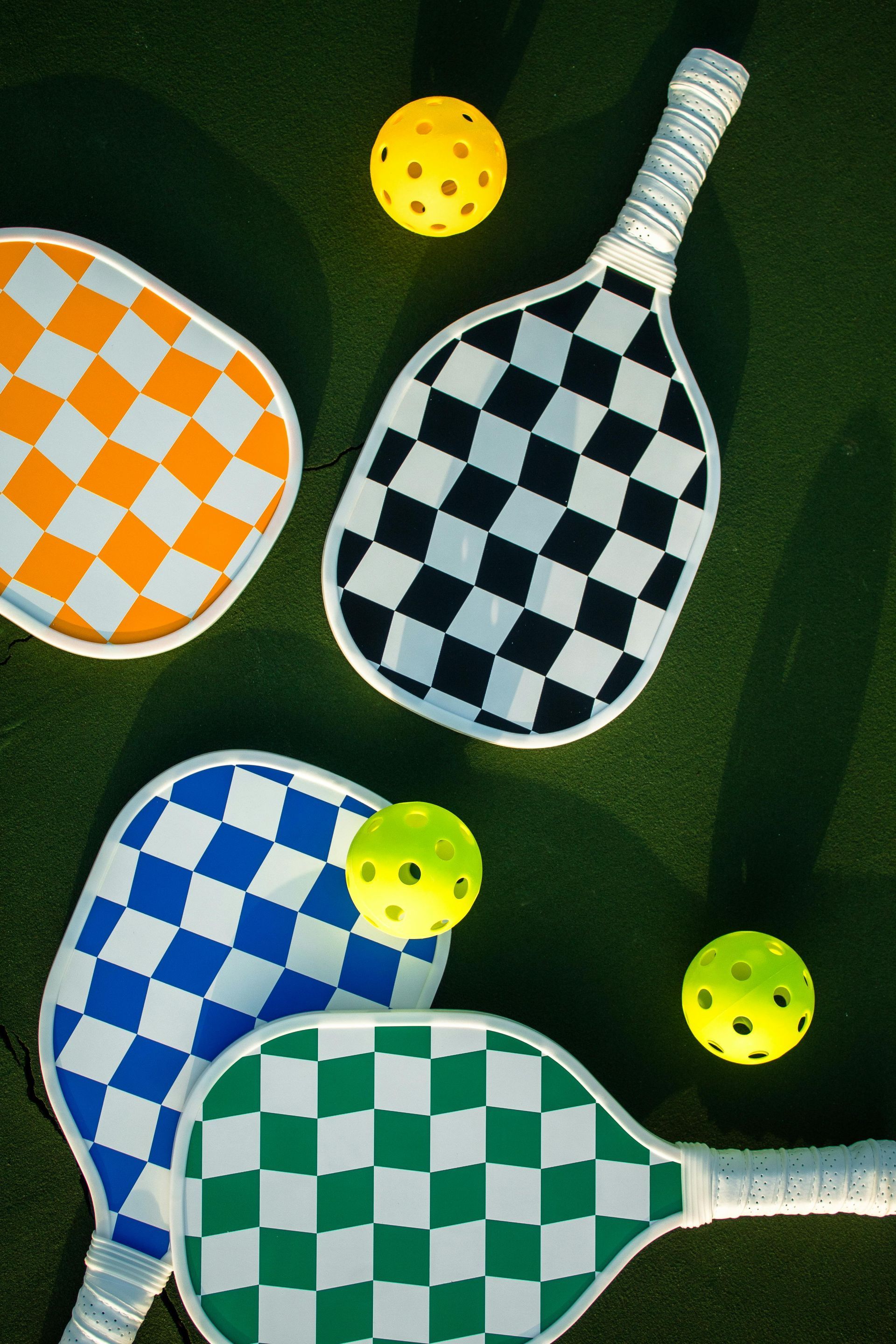 Four colorful pickleball paddles and balls on a dark green background