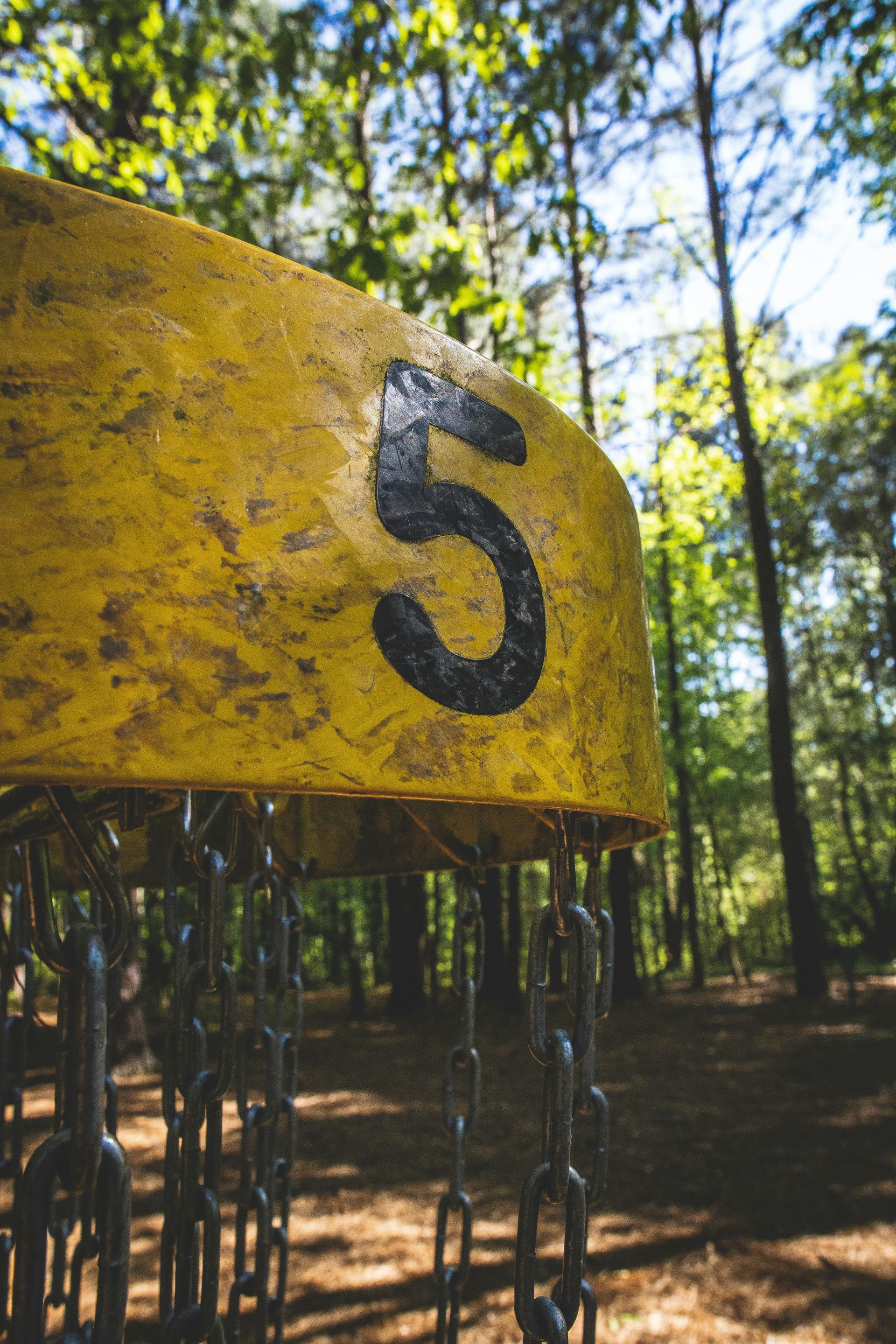 Yellow disc golf basket marked with a black number 5 in a wooded outdoor course