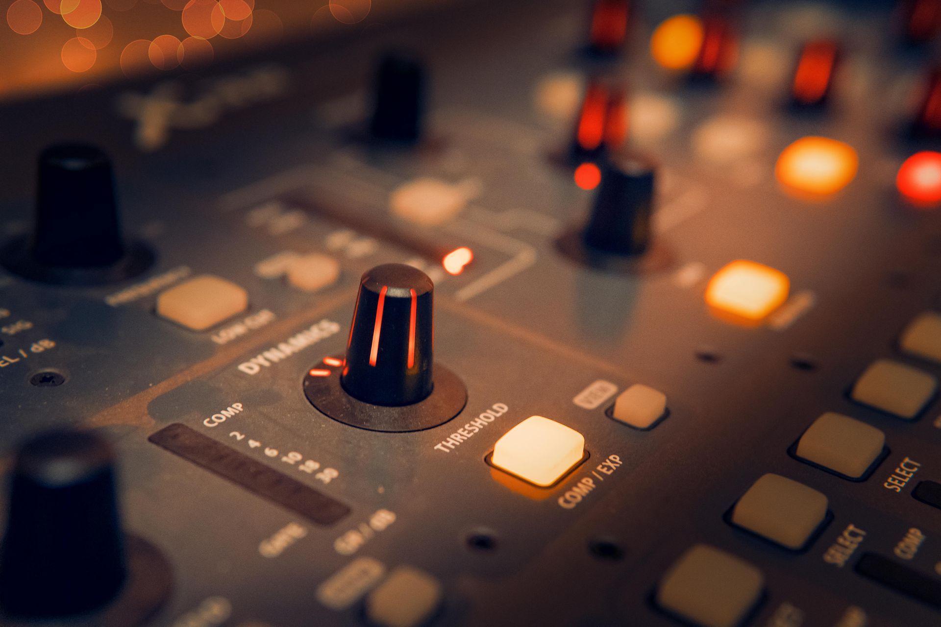 Close-up of a dark audio mixing console with glowing orange buttons and knobs
