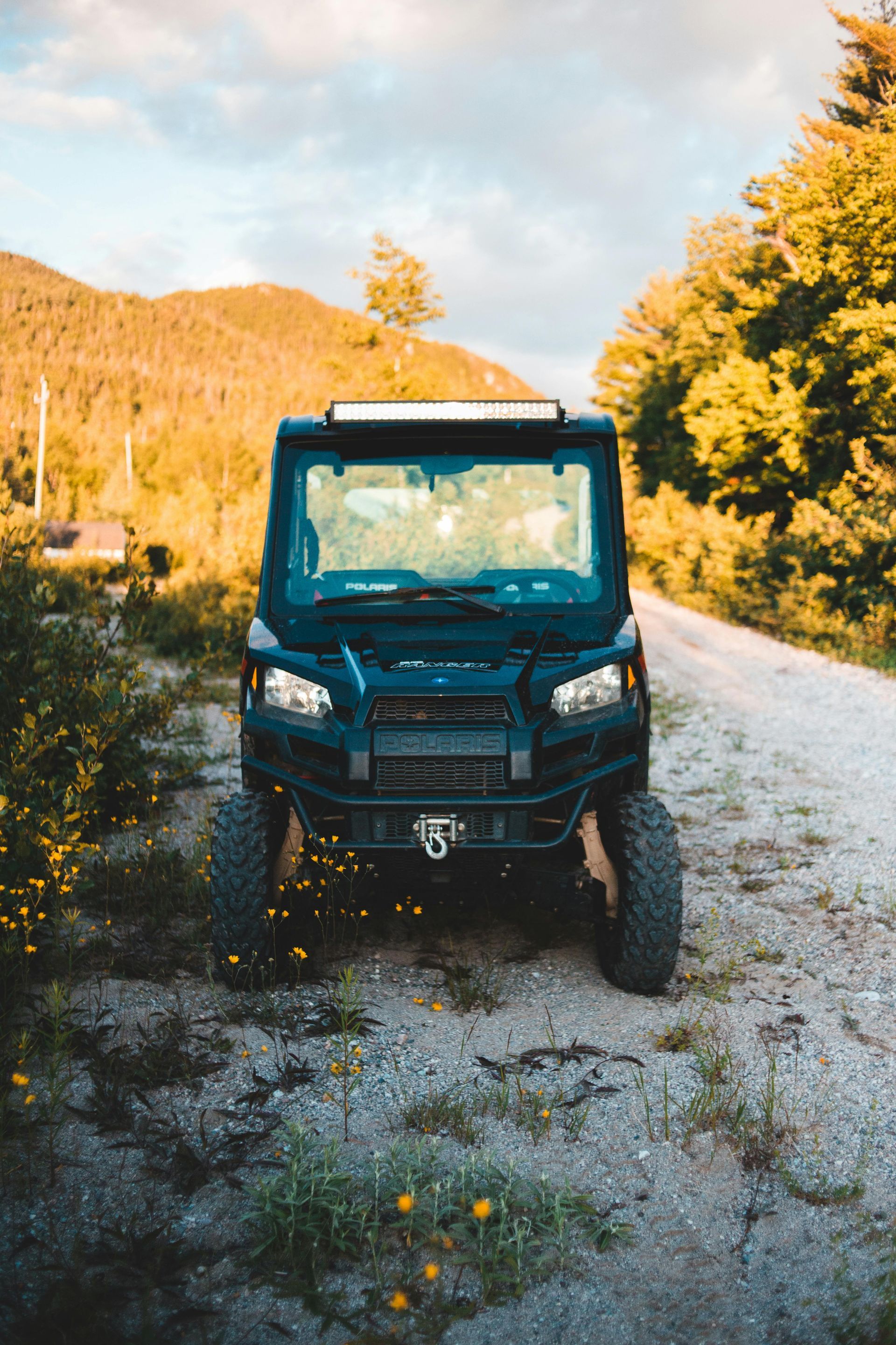 Blue off-road utility vehicle on a gravel path beside autumn trees and hills under a bright sky