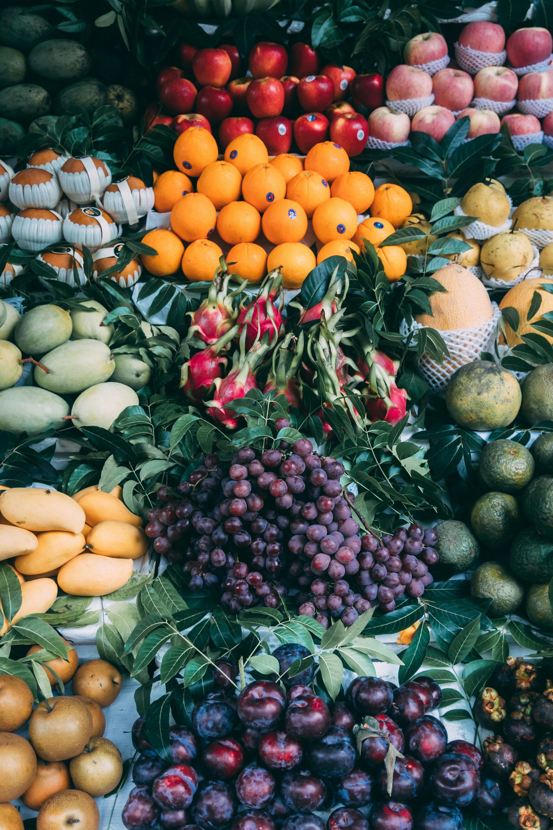 Assortment of fresh fruits: apples, oranges, mangoes, grapes, plums, and dragon fruit arranged for sale.