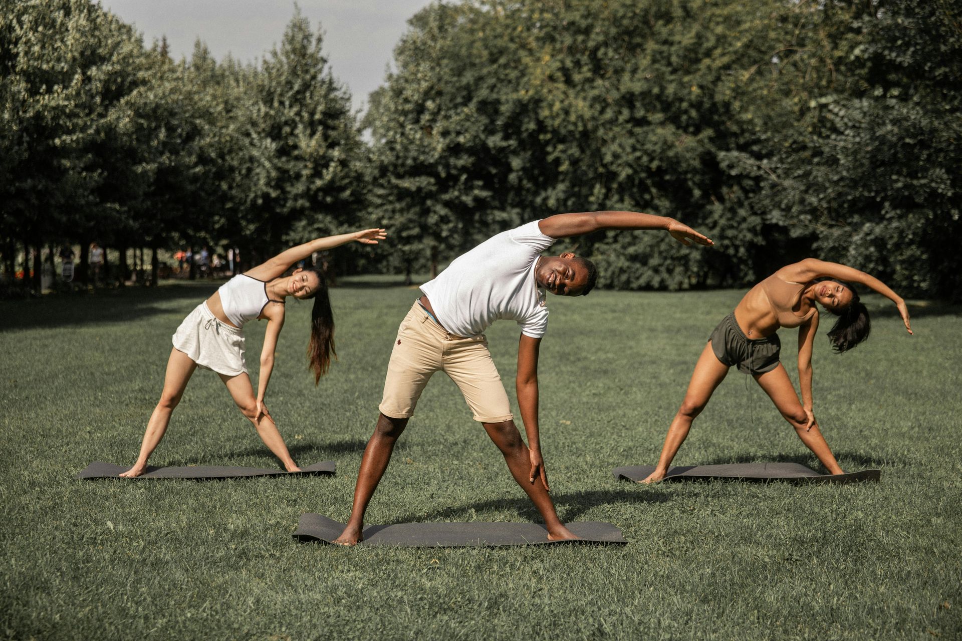 Three people stretching sideways on a grassy field in a park
