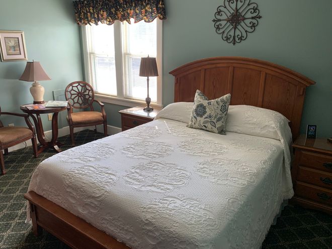 Cozy bedroom with a wooden bed, white quilt, teal walls, and a window seat by the window