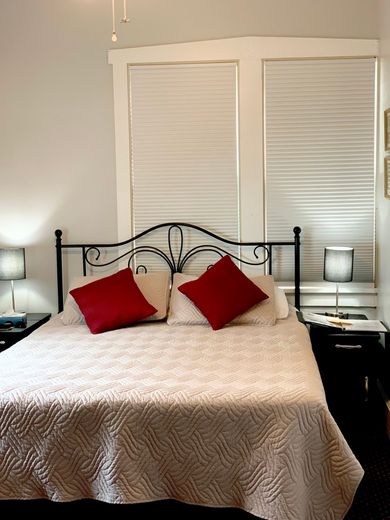 Bedroom with made bed, red pillows, black metal headboard, and two bedside lamps before white blinds.
