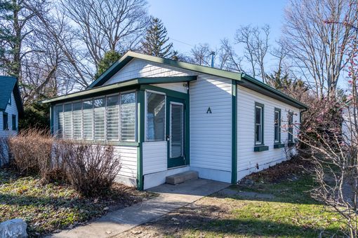 Small white house with green trim and screened porch, surrounded by trees in a yard.