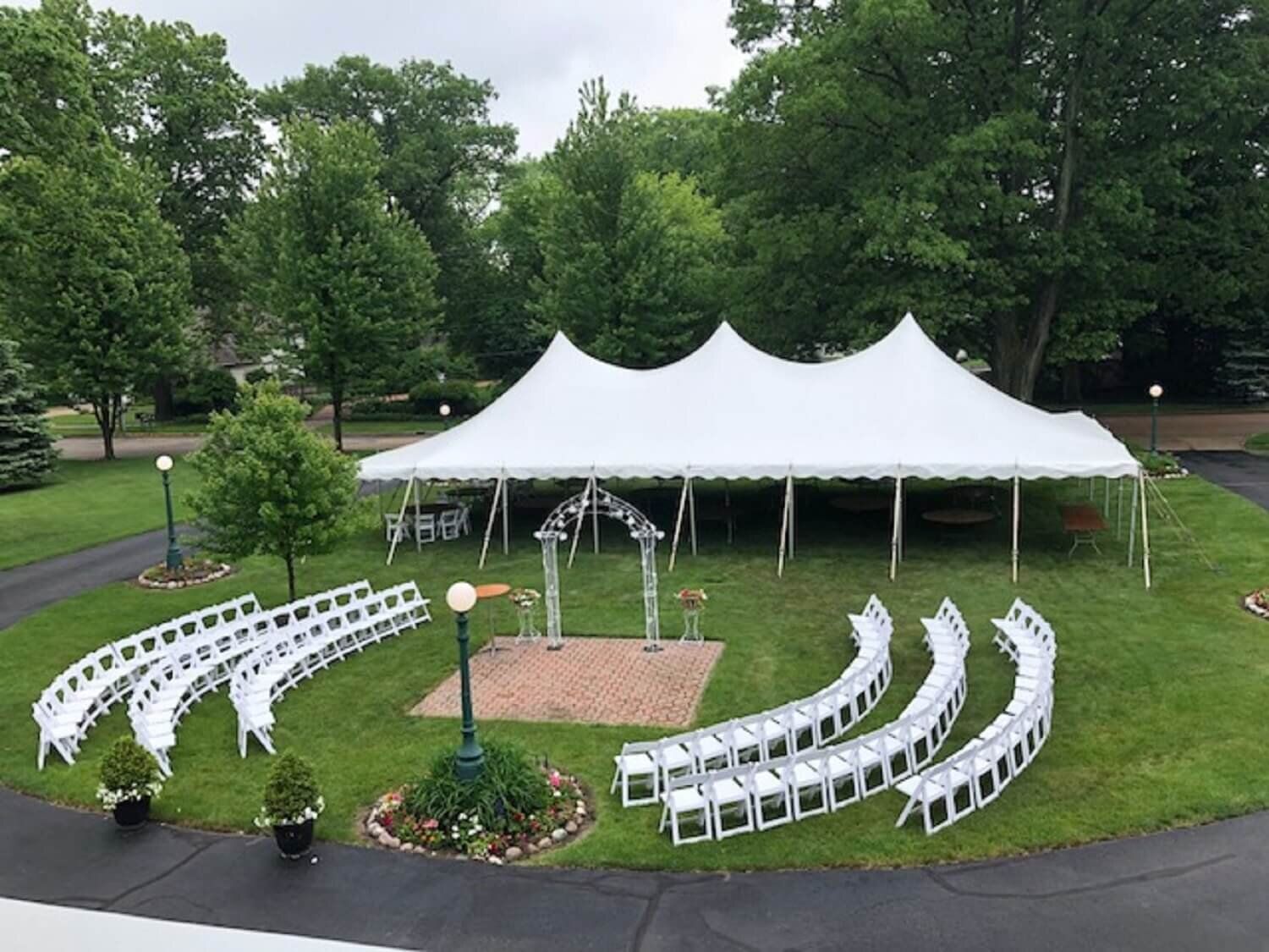 White event tent with curved rows of white chairs on a grassy lawn in a park