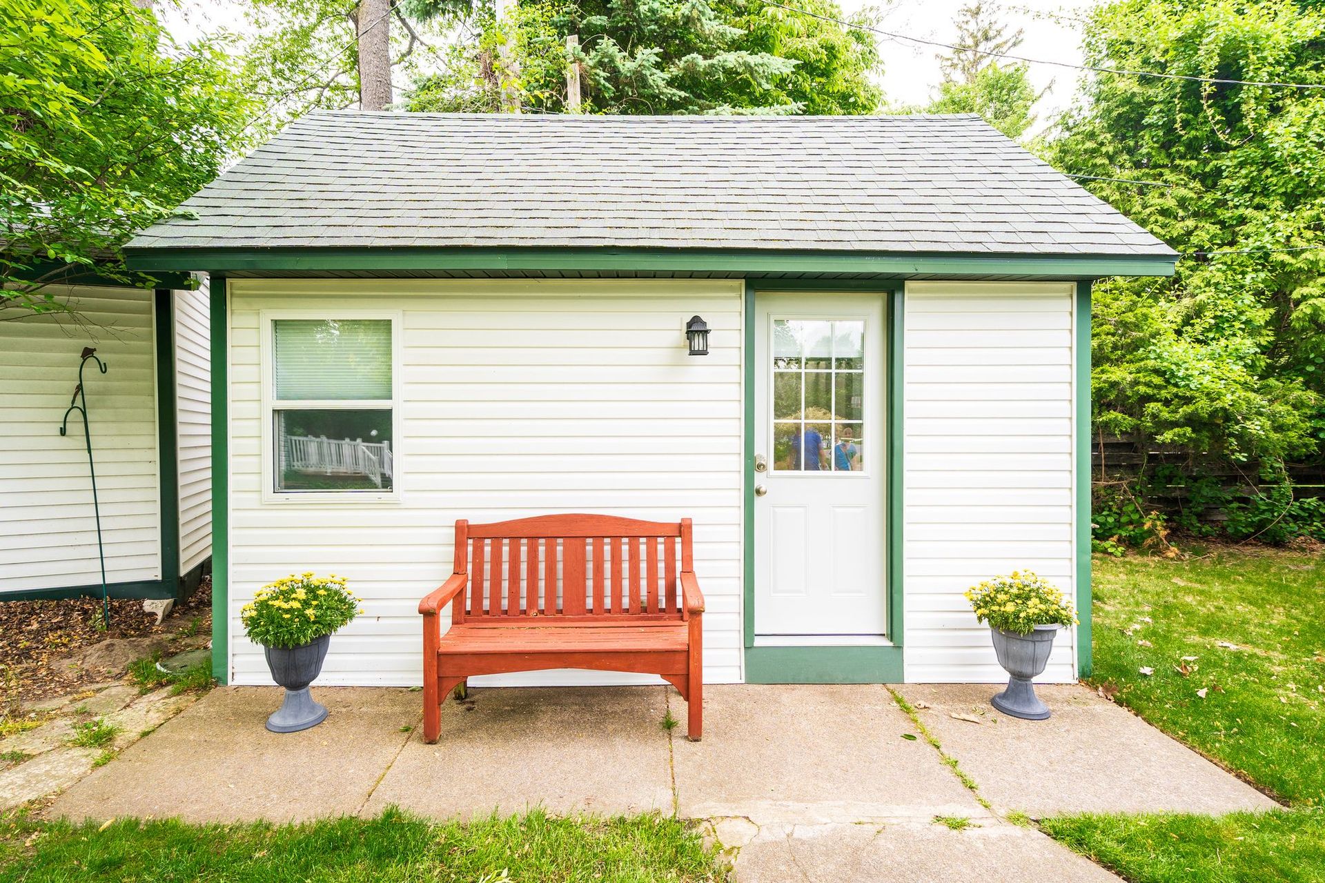 Small white cottage with green trim, a wooden bench, and potted plants on a front patio