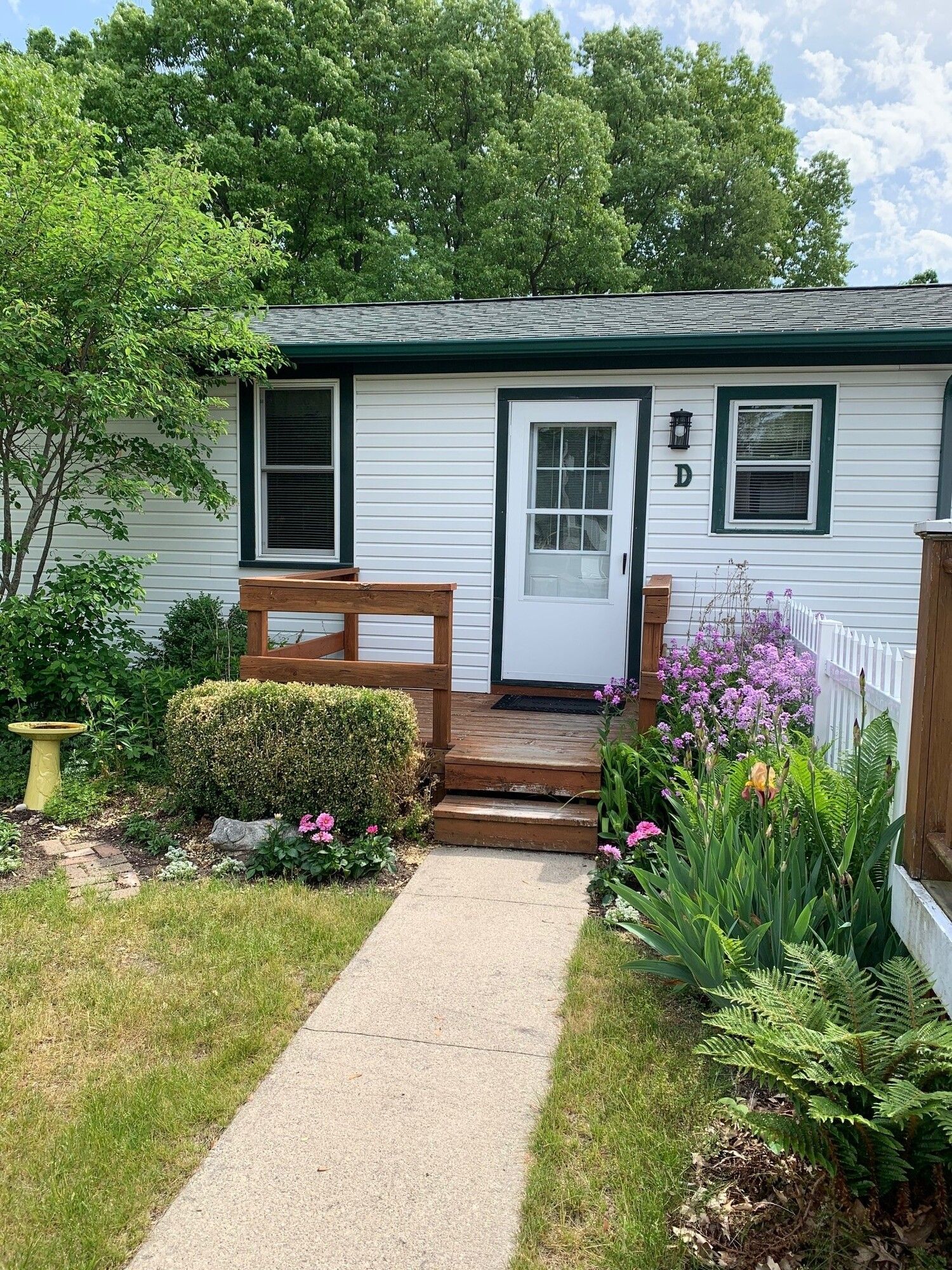 Small white house with a front walkway, wooden steps, and colorful flower beds in the garden