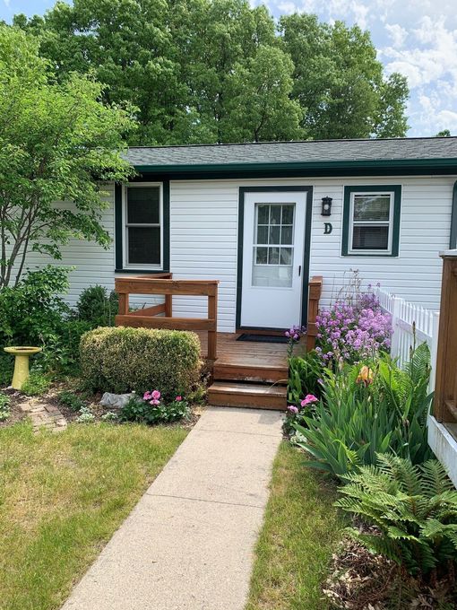 Small white house with a front walkway, wooden steps, and colorful flower beds in the garden