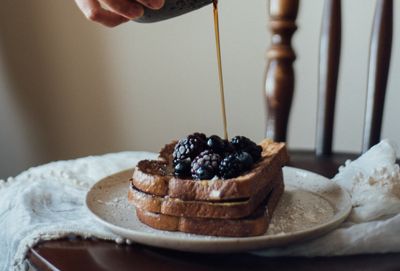 Stacked French toast topped with blueberries as syrup is poured over it on a plate