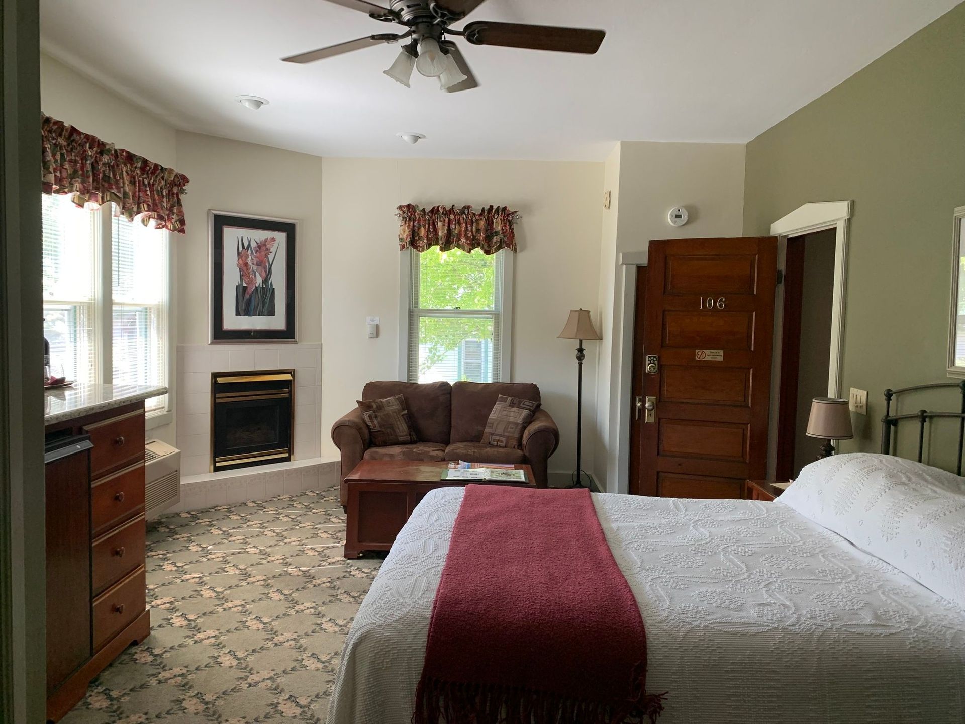 Bedroom with bed, armchair, fireplace, and large windows in a cozy, carpeted room