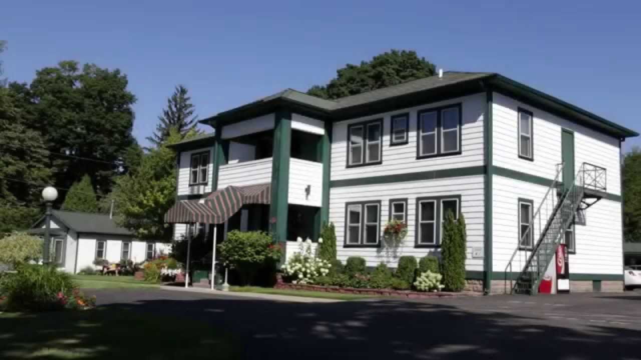 White two-story house with green trim, front porch, and steps beside a tree-lined driveway.