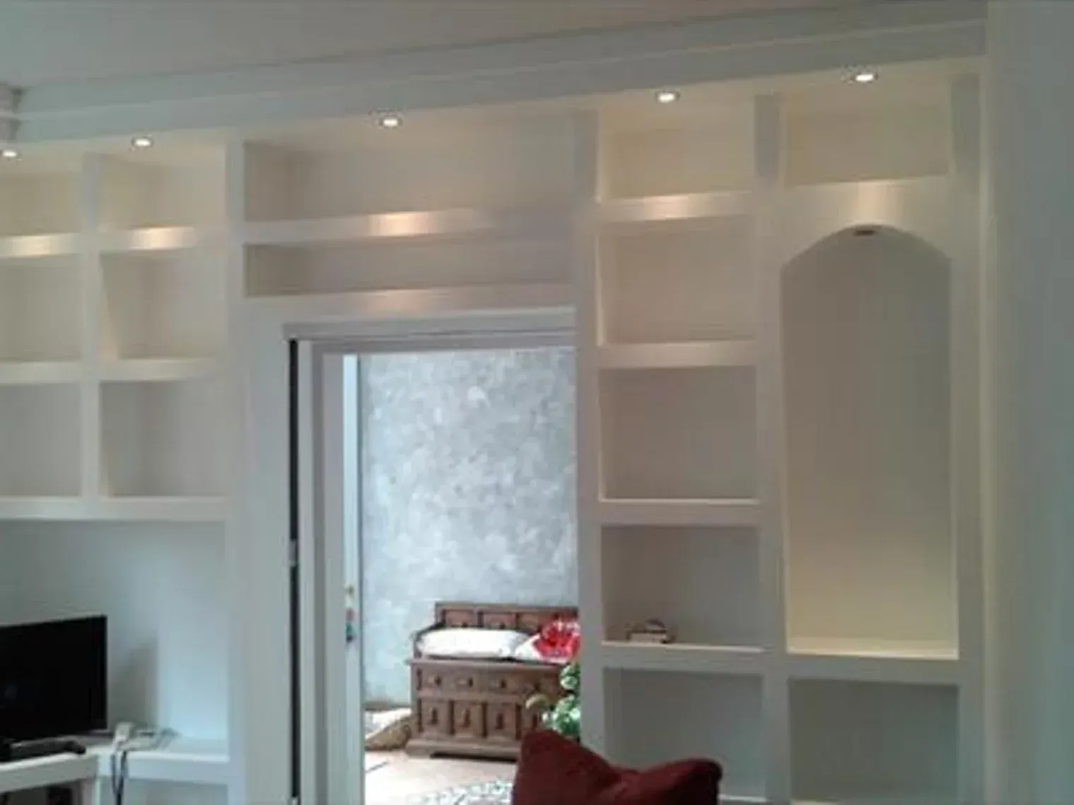 Scaffale bianco a muro con illuminazione interna e arco. Al centro è visibile una porta.