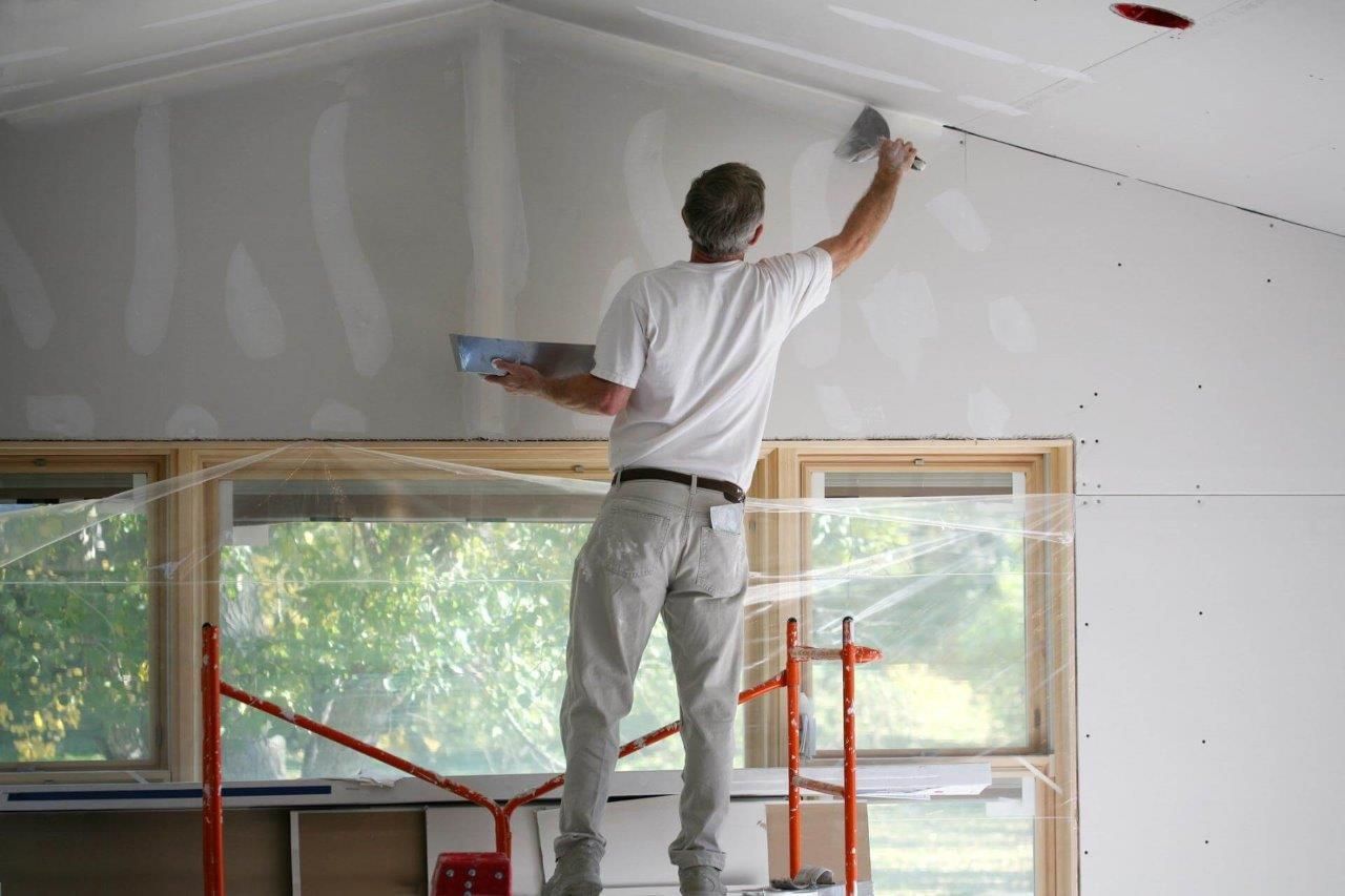 Persona su un'impalcatura che applica il composto per cartongesso al soffitto di una stanza in costruzione.