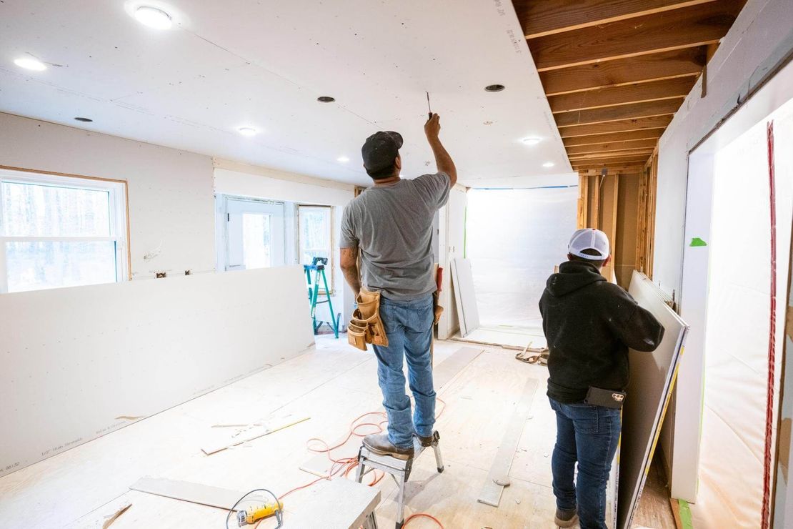 Due operai edili installano cartongesso sul soffitto di una stanza.