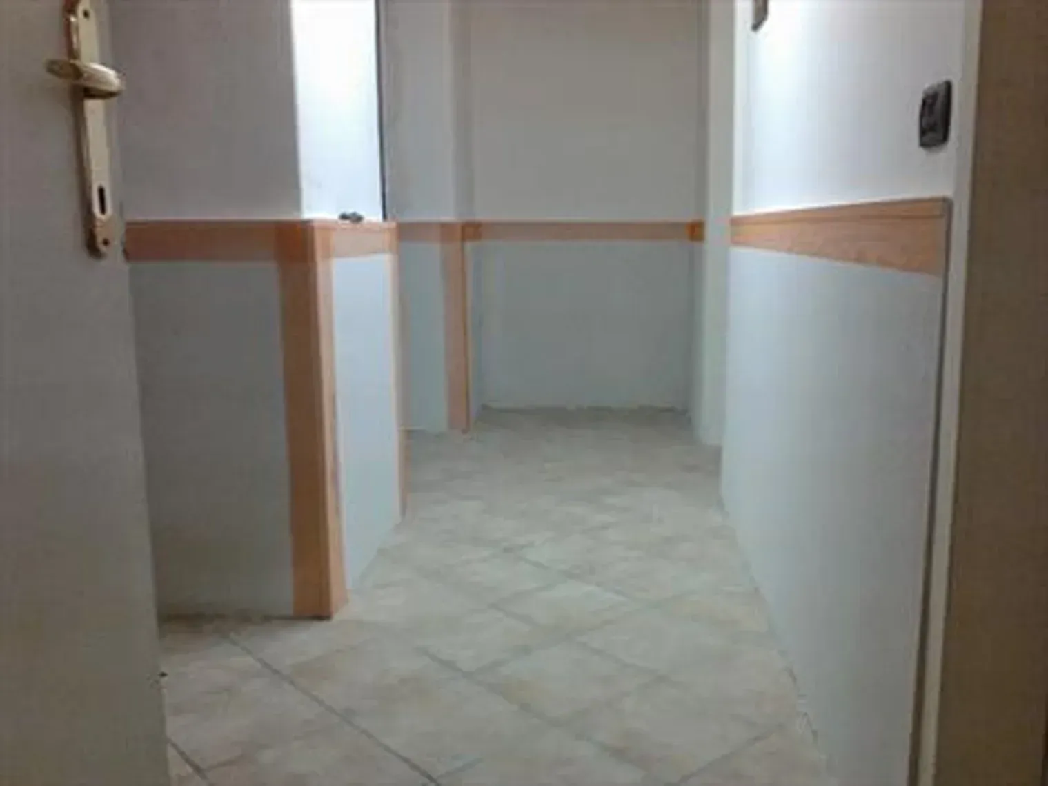 Stanza vuota con pavimento piastrellato, pareti e finiture bianche, con una porta aperta.