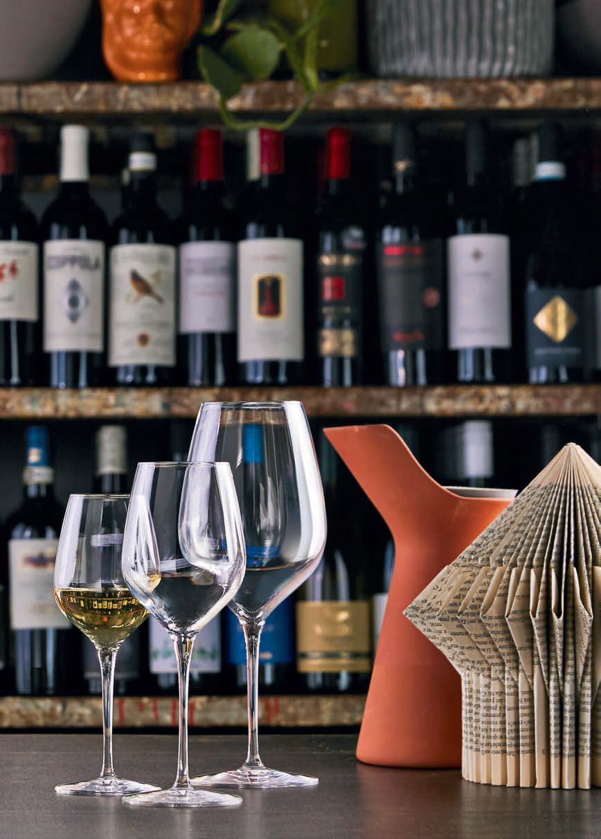 Calici da vino e vasi decorativi su un tavolo davanti a un'esposizione di bottiglie di vino.