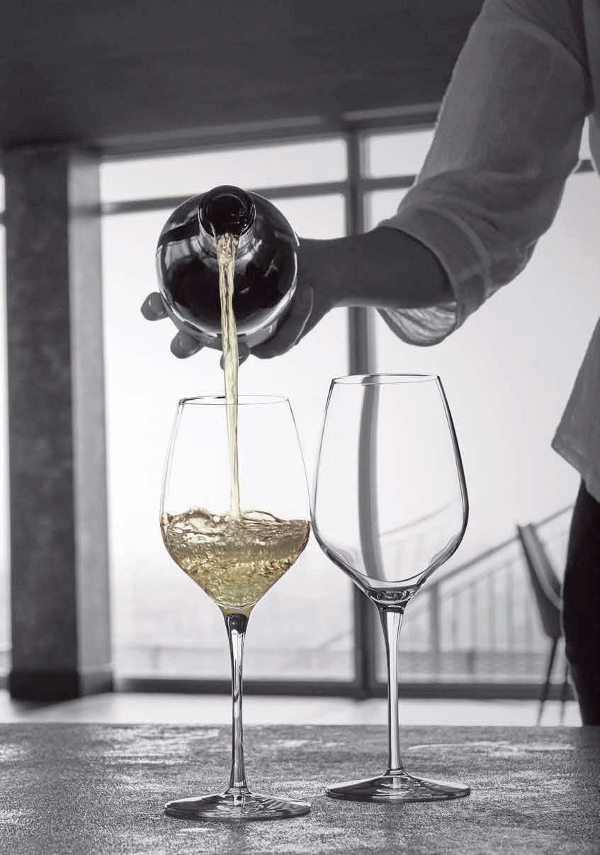 Una mano versa del vino bianco in un bicchiere accanto a un bicchiere vuoto su un tavolo.