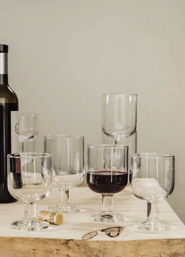 Tavola apparecchiata con vari calici da vino e una bottiglia di vino rosso su una tovaglia bianca.