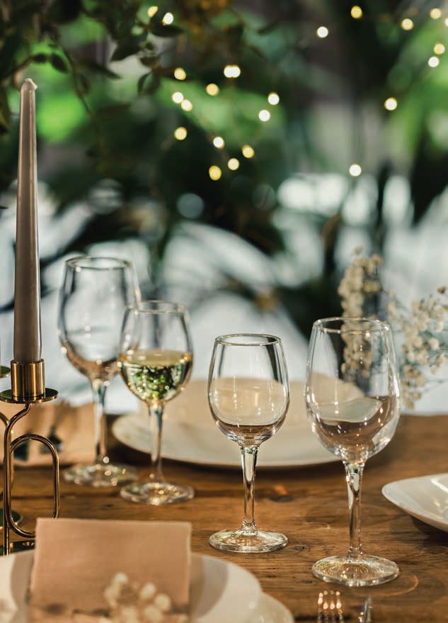 Elegante apparecchiatura della tavola con calici da vino, candela e decorazioni floreali sotto una morbida luce bokeh.