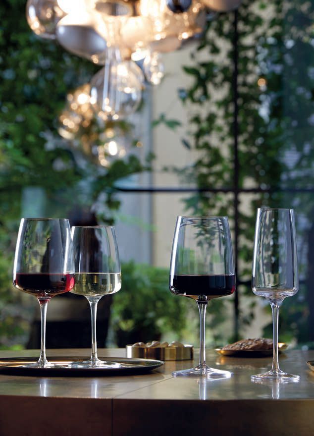 Calici da vino su un tavolo durante un'elegante cena all'aperto, immersi nel verde e illuminati da luci soffuse.