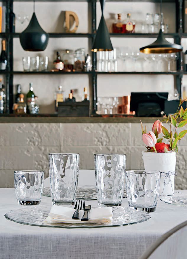 In un ristorante moderno, la tavola è apparecchiata con bicchieri trasparenti, piatti bianchi e una piccola composizione floreale.